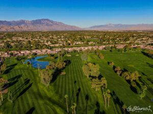 Aerial view of the golf course and pond, with suburbs at the border and mountains in the distance.