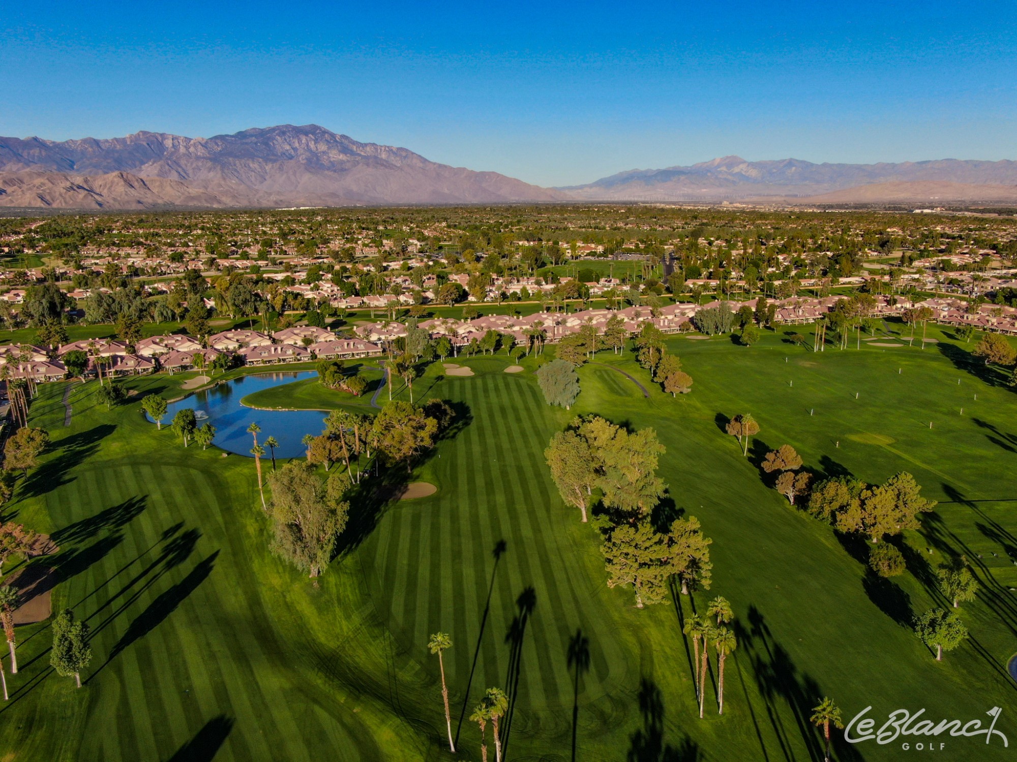 Aerial view of the golf course and pond, with suburbs at the border and mountains in the distance.