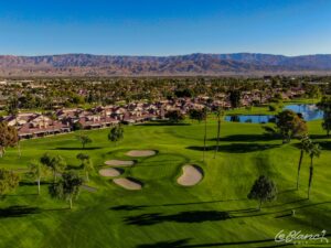 Aerial view of the golf course and pond, with suburbs at the border and mountains in the distance.