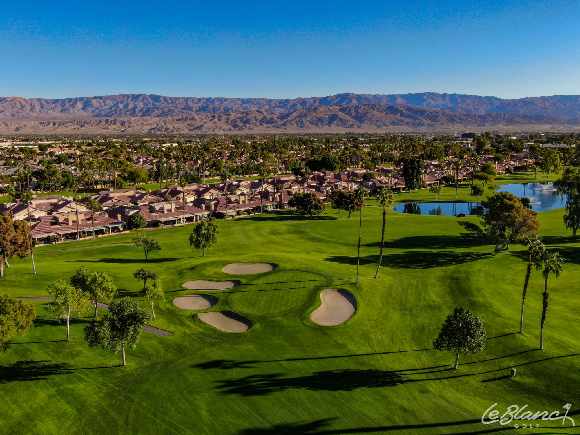 Aerial view of the golf course and pond, with suburbs at the border and mountains in the distance.