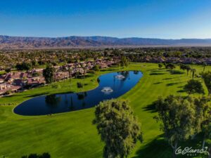 Aerial view of the golf course and pond, with suburbs at the border and mountains in the distance.