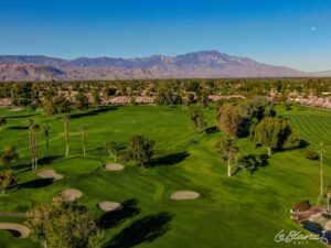 Aerial view of the golf course, driving range, and pond, with suburbs at the border and mountains in the distance.