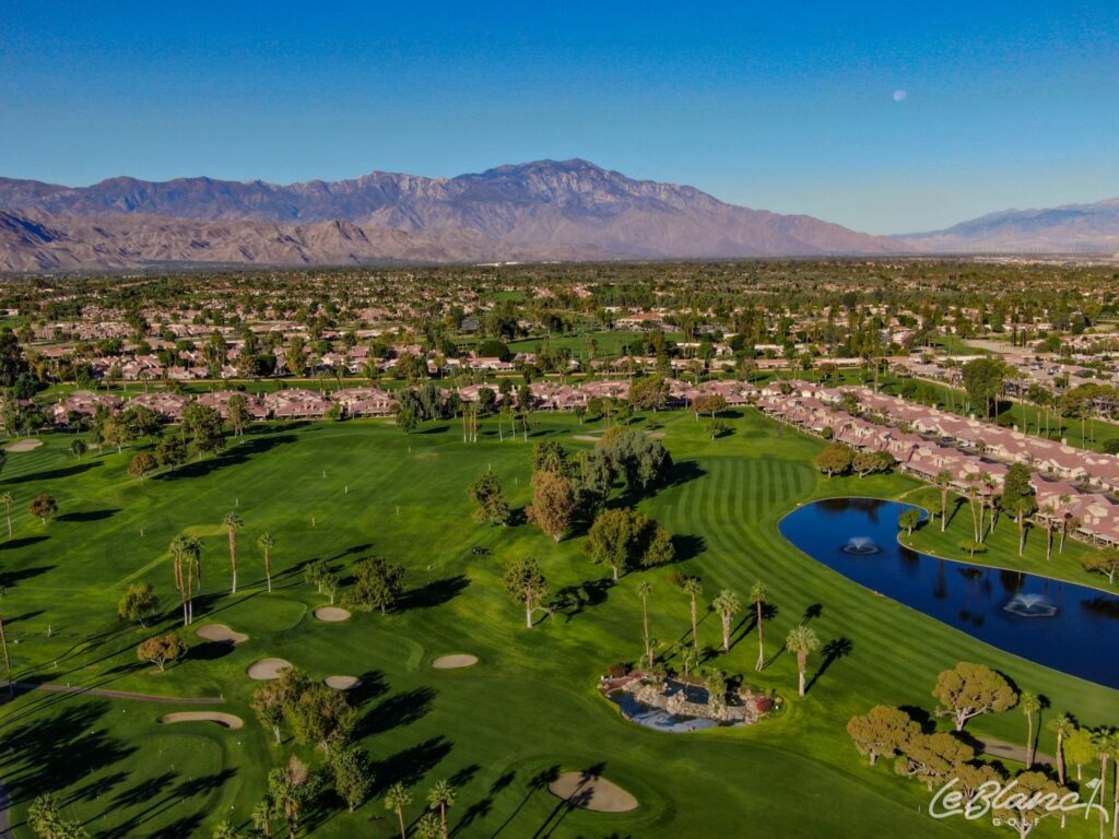 Aerial view of the golf course, driving range, and pond, with suburbs at the border and mountains in the distance.