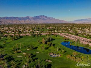 Aerial view of the golf course, driving range, and pond, with suburbs at the border and mountains in the distance.