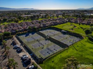 Aerial view of 8 tennis courts surrounded by the golf course on one side and a sunny neighborhood on the other.