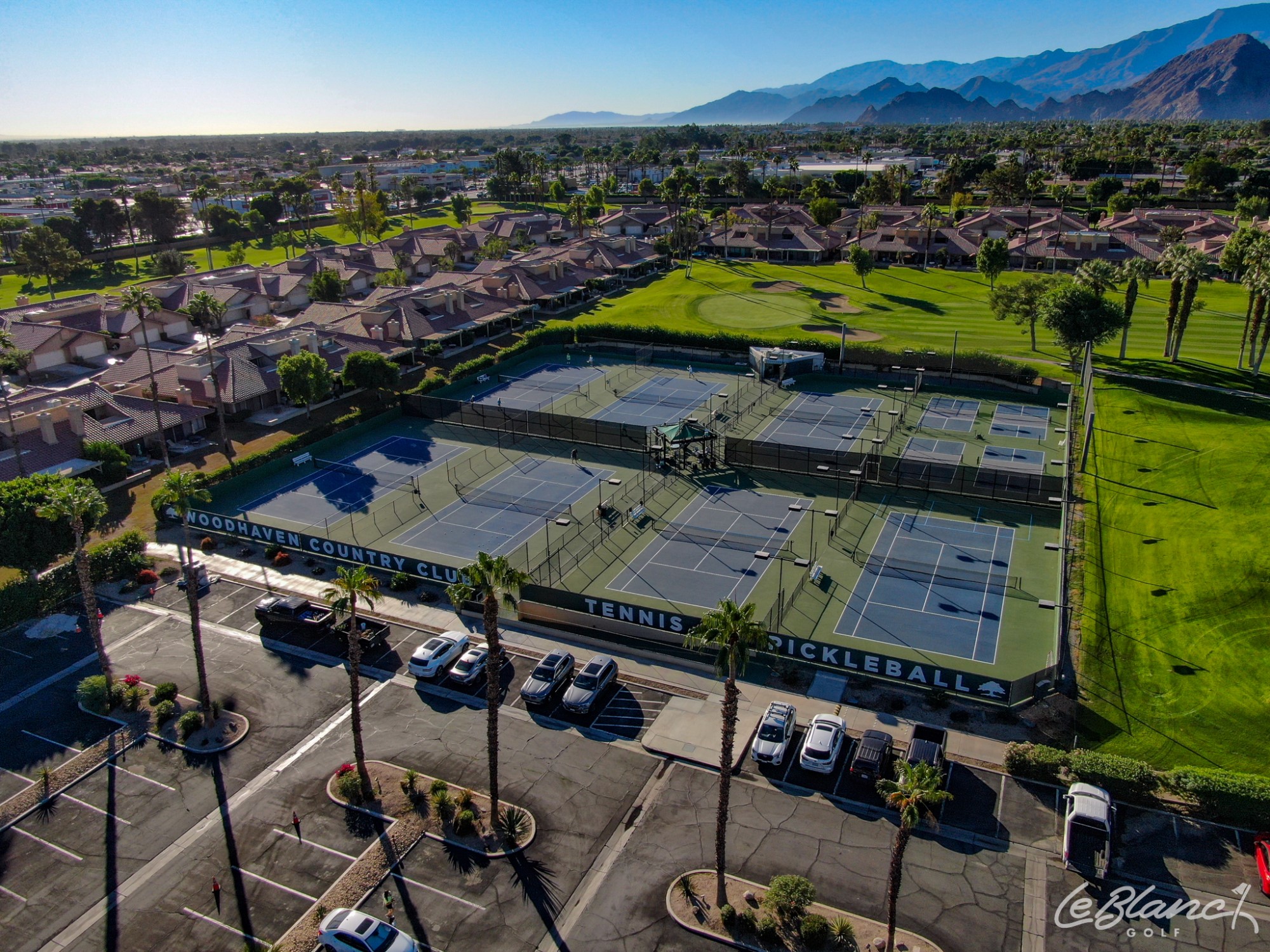Aerial view of 8 tennis courts surrounded by the golf course on one side and a sunny neighborhood on the other.