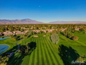 Aerial view of immaculate fairway with suburbs just beyond and mountains in the distance.